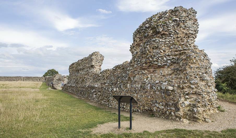 The surviving flint and mortar walls of Burgh Castle Roman fort standing above open grassland