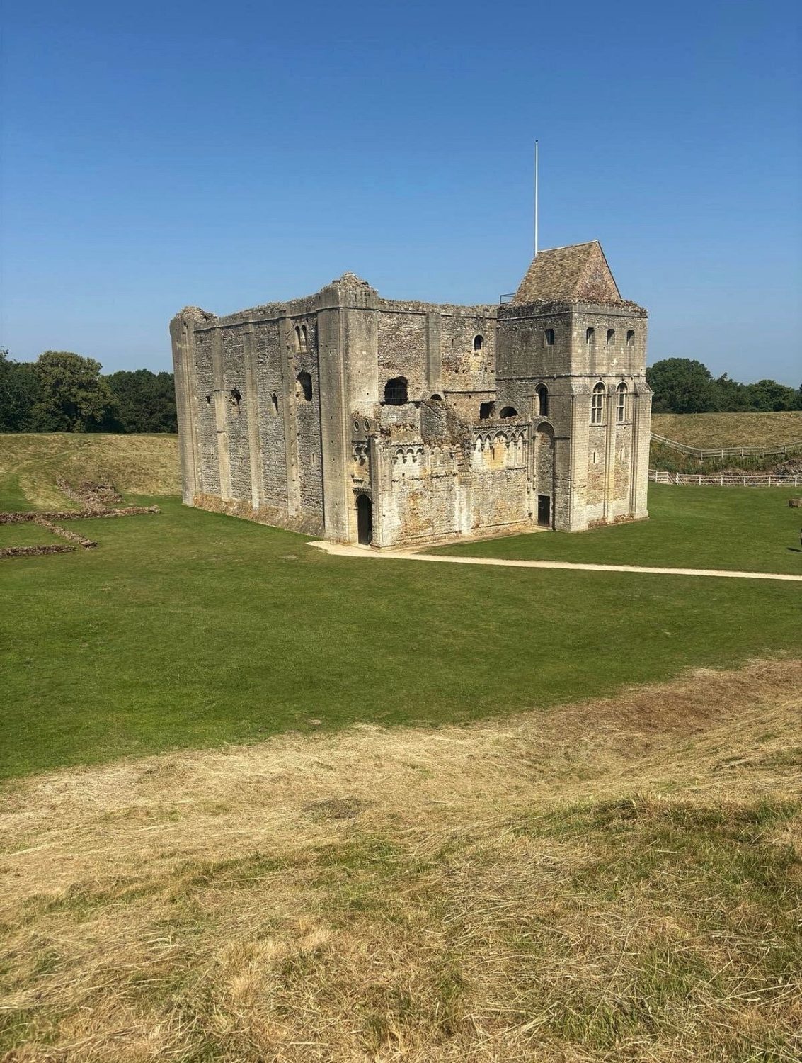 The Norman stone keep at Castle Rising standing on mown grass surrounded by earthworks
