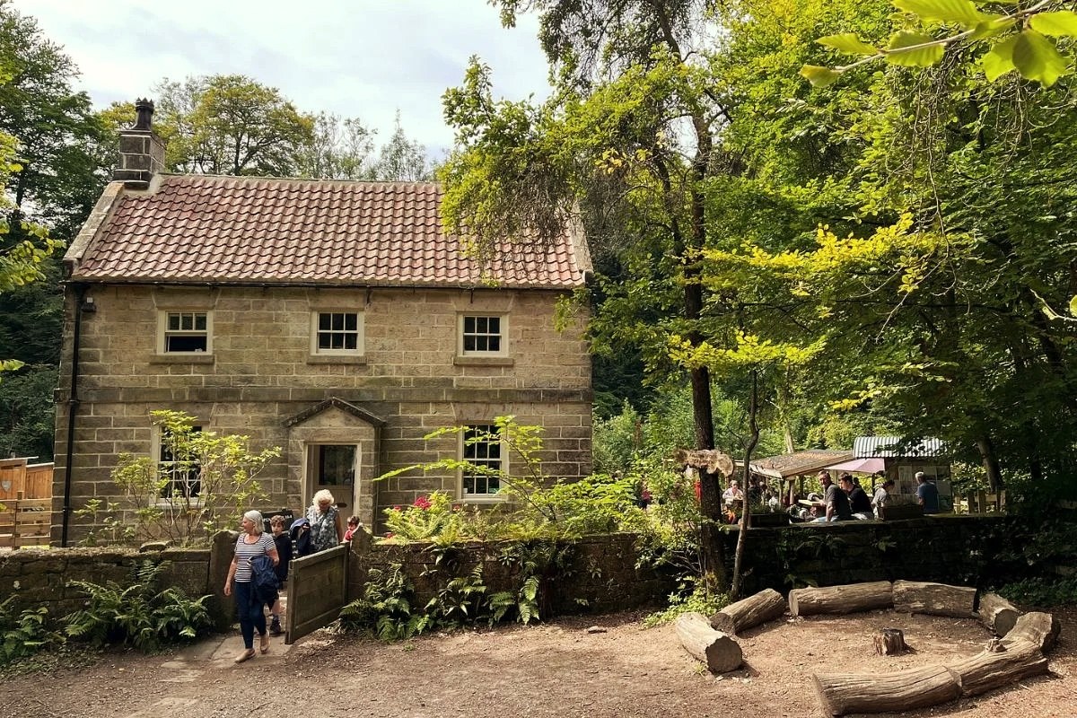 The stone cottage at Midge Hall with the Falling Foss Tea Garden's outdoor tables under the trees beside it