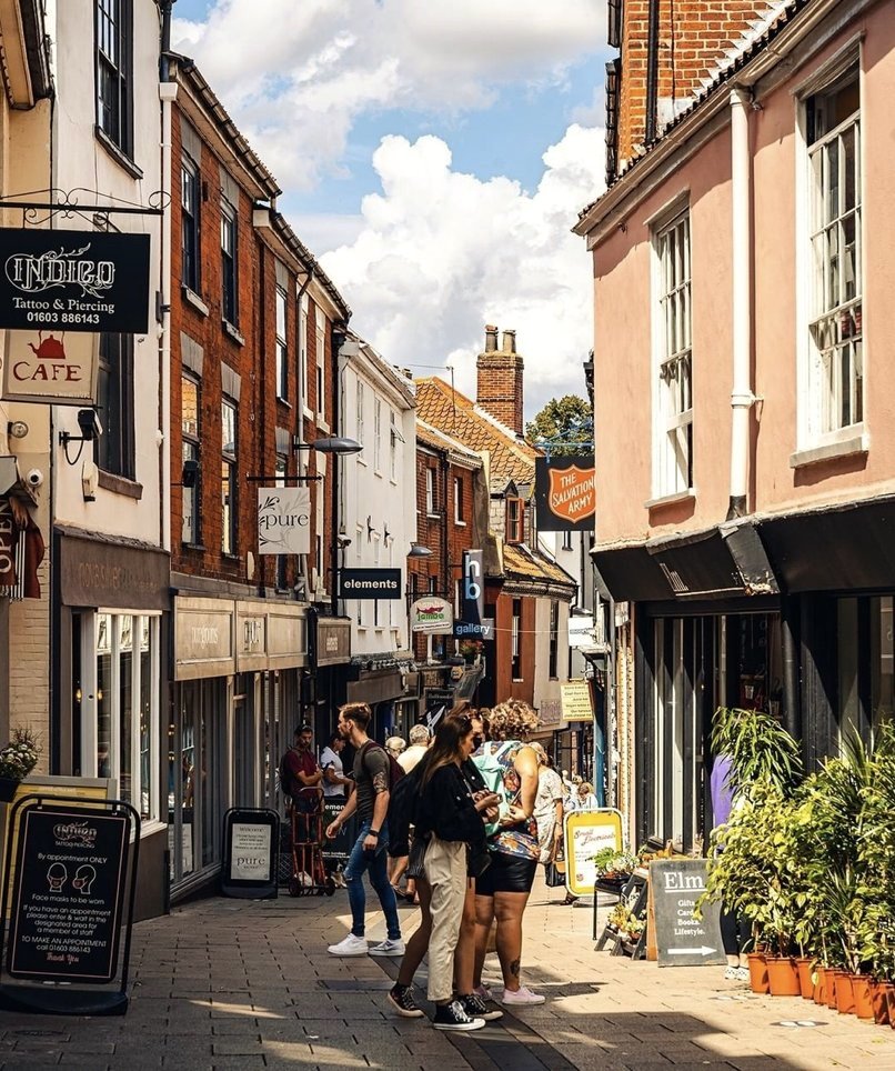 A narrow street in the Norwich Lanes lined with independent shops and cafes, people walking between them