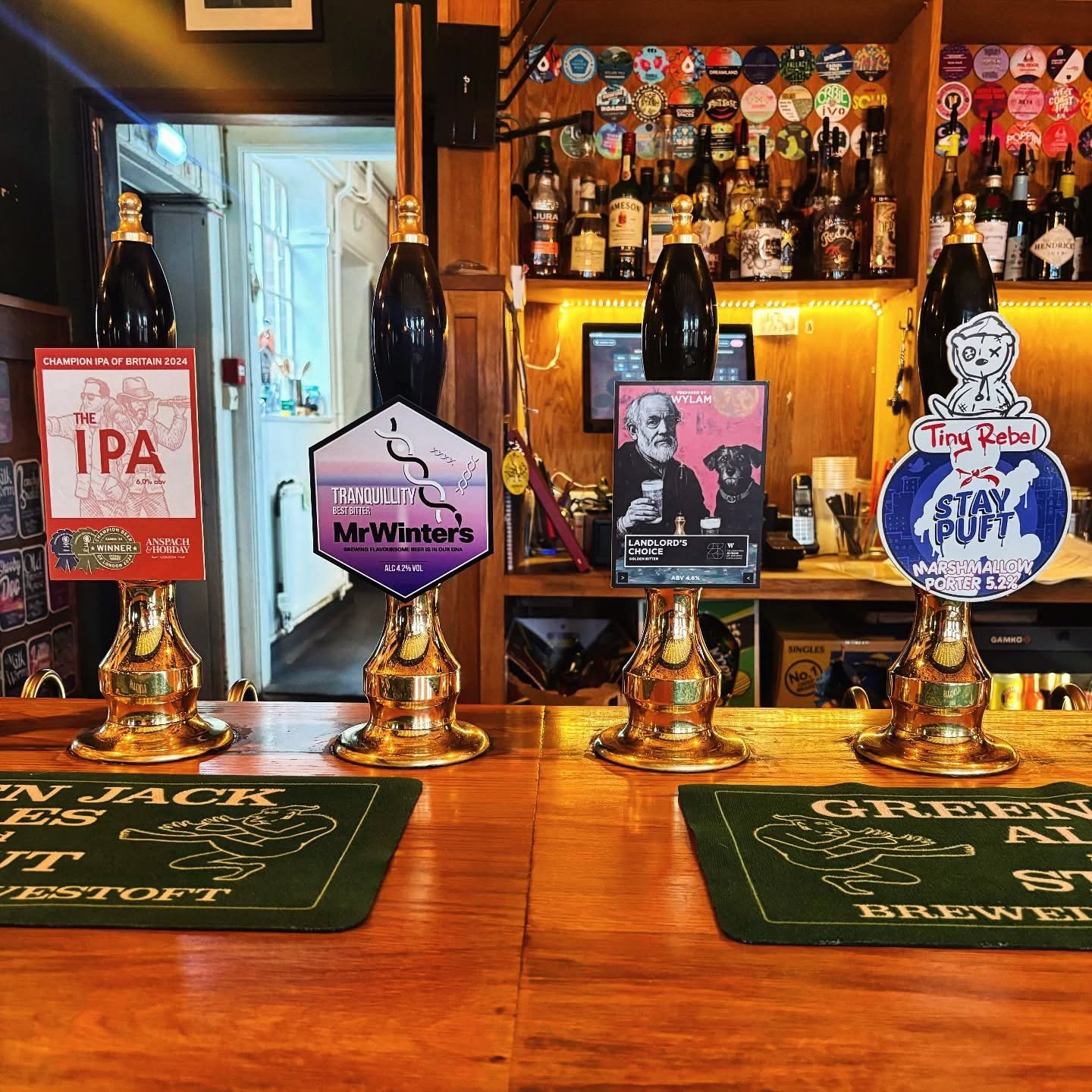 Four hand pulls on the bar at the Artichoke in Norwich, with pump clips covering the wall behind