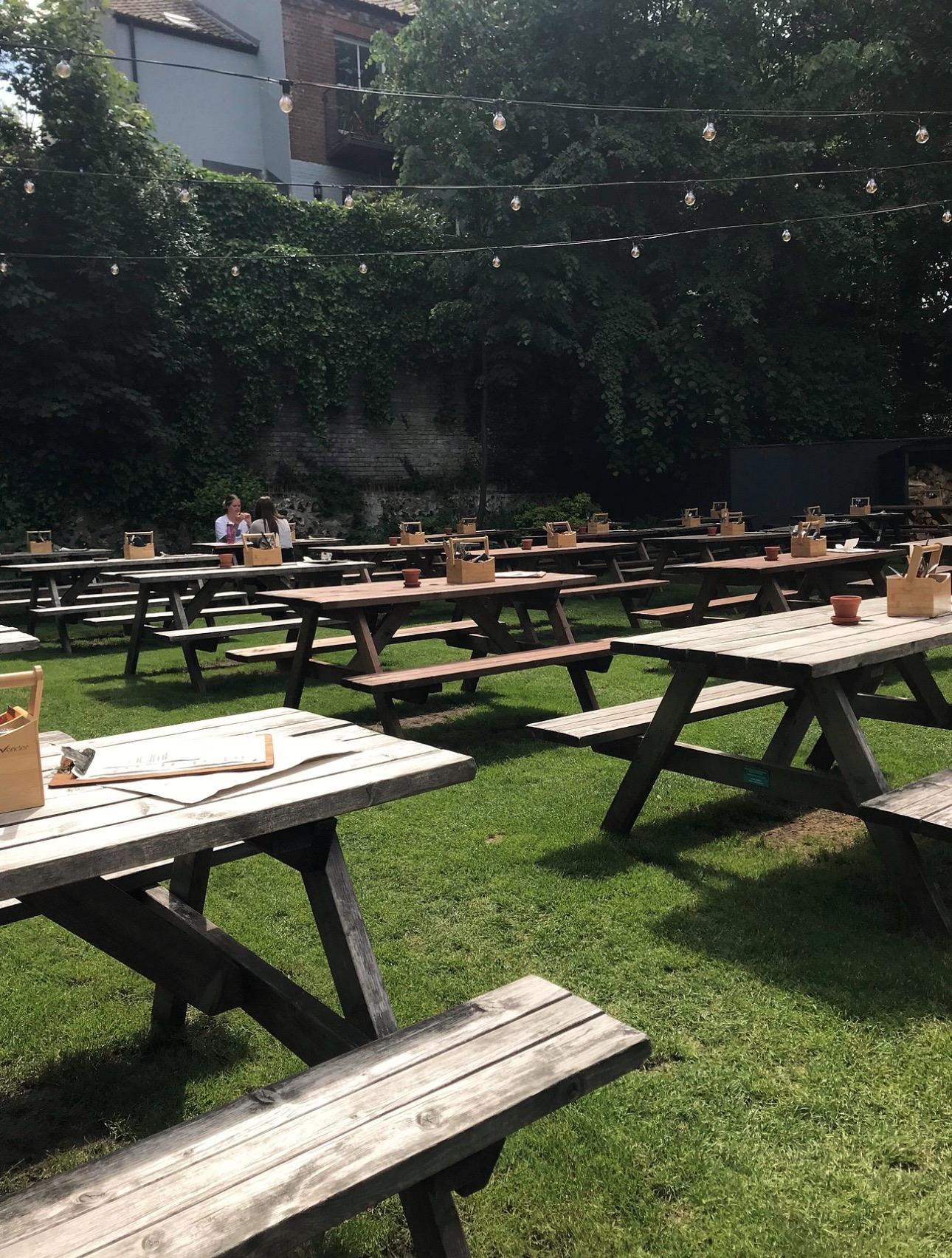 The garden at the Black Horse on Earlham Road, Norwich, rows of picnic tables on grass under festoon lights