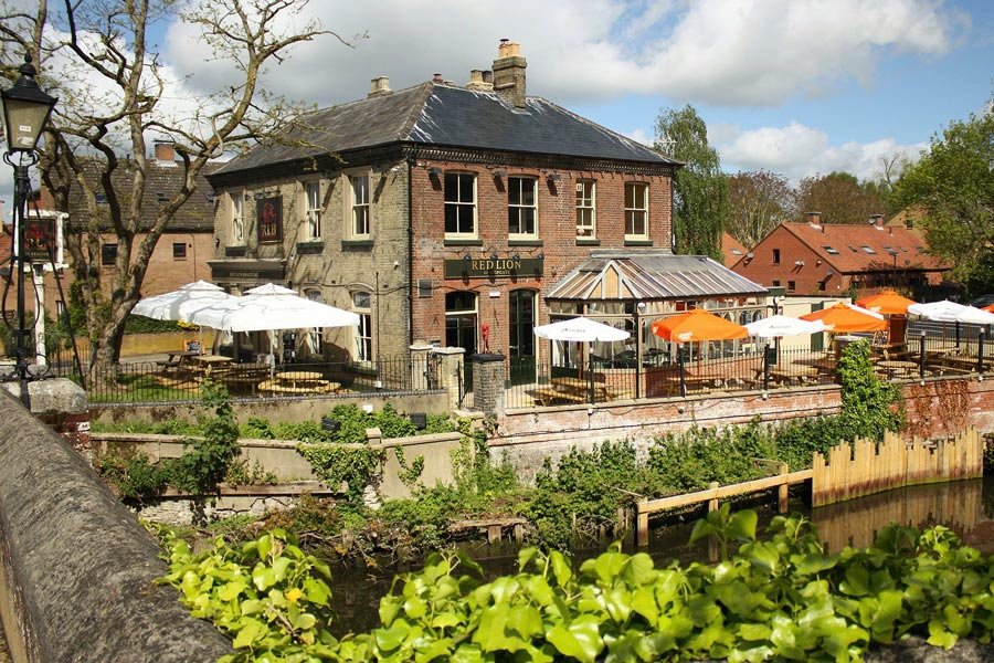 The Red Lion at Bishopgate in Norwich seen from across the Wensum, parasols set out on the riverside terrace