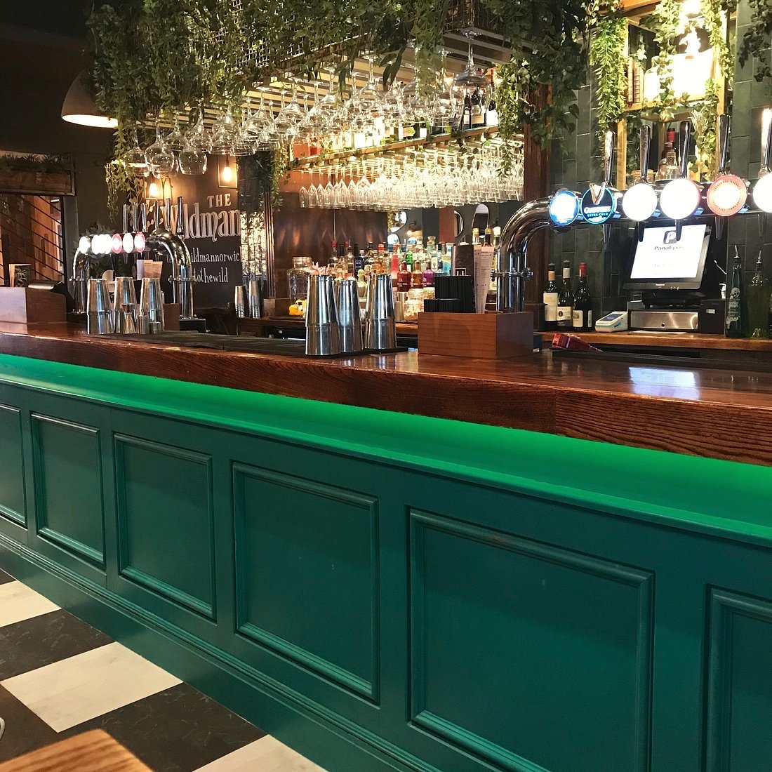 The bar at the Wildman in Norwich, deep green panelling with glassware hung above and cocktail shakers lined up
