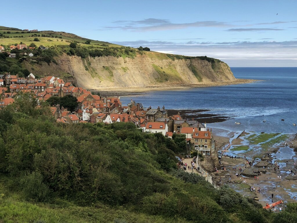Robin Hood's Bay seen from the Cleveland Way above, red rooftops packed down to the shore with the cliff curving away beyond