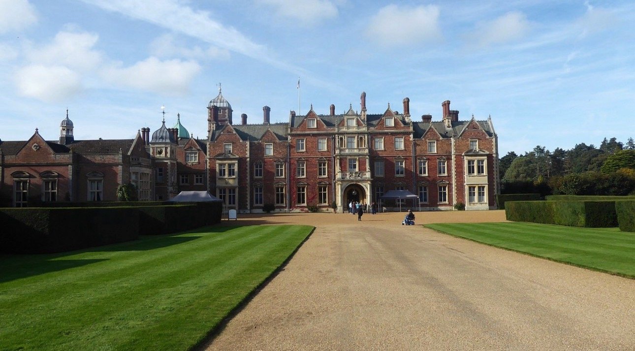 The front of Sandringham House in Norfolk, red brick with striped lawns leading up to the entrance