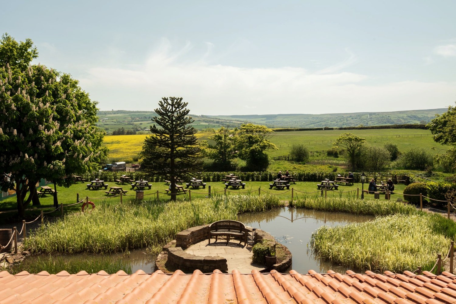 The garden and pond at The Stables at Cross Butts, with picnic benches on the lawn and open countryside beyond