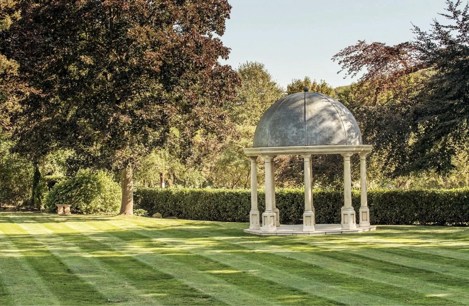 A domed stone rotunda on a striped lawn at Wentbridge House, framed by mature trees