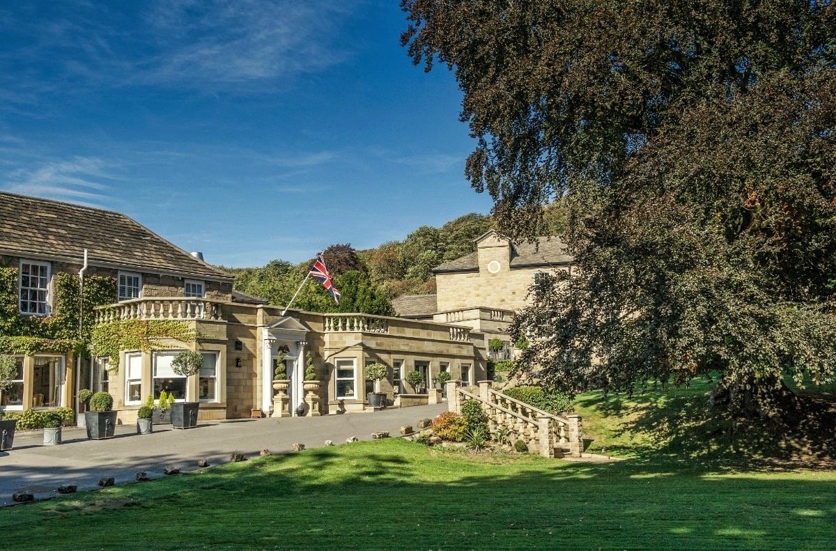 The stone frontage of Wentbridge House Hotel with a flag flying, wooded valley slope rising behind it